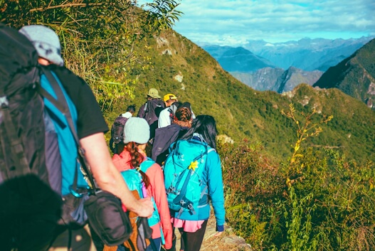 Grupo de trekking numa trilha montanhosa com mochilas e equipamentos de aventura